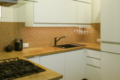 Foto på ett litet skandinaviskt kök, med en nedsänkt diskho, släta luckor, vita skåp, träbänkskiva, orange stänkskydd, stänkskydd i mosaik, svarta vitvaror, mellanmörkt trägolv och beiget golv