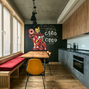 This is an example of an industrial single-wall eat-in kitchen in Moscow with a drop-in sink, flat-panel cabinets, grey cabinets, white splashback, stainless steel appliances, medium hardwood floors, brown floor, black benchtop, no island and recessed.