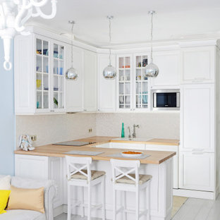 Immagine di una cucina classica con lavello da incasso, ante con bugna sagomata, ante bianche, top in legno, paraspruzzi bianco, elettrodomestici in acciaio inossidabile, pavimento in legno verniciato, penisola, pavimento bianco e top marrone