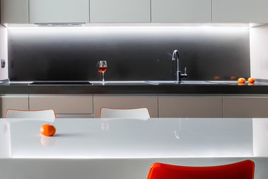 Идея дизайна: прямая кухня в современном стиле с обеденным столом, белыми фасадами, столешницей из акрилового камня и черным фартуком