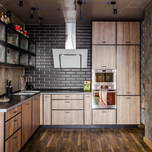 Photo of an industrial l-shaped open plan kitchen in Other with flat-panel cabinets, medium wood cabinets, black splashback, subway tile splashback, stainless steel appliances, dark hardwood floors, no island, brown floor, a double-bowl sink and stainless steel benchtops.