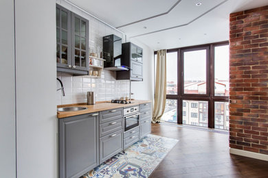 Стильный дизайн: кухня-гостиная в современном стиле с накладной мойкой, фасадами с выступающей филенкой, серыми фасадами, белым фартуком и коричневой столешницей без острова - последний тренд
