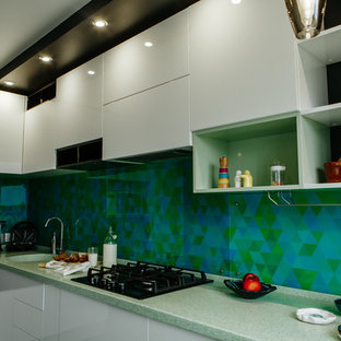 Mid-sized contemporary l-shaped separate kitchen in Other with an integrated sink, flat-panel cabinets, white cabinets, solid surface benchtops, green splashback, glass tile splashback, stainless steel appliances, laminate floors, no island, black floor and turquoise benchtop.