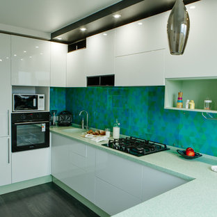 Design ideas for a mid-sized contemporary l-shaped separate kitchen in Other with an integrated sink, flat-panel cabinets, white cabinets, solid surface benchtops, green splashback, glass tile splashback, stainless steel appliances, laminate floors, no island, black floor and turquoise benchtop.