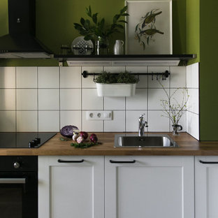 Ispirazione per una cucina nordica di medie dimensioni con lavello sottopiano, ante con bugna sagomata, ante bianche, top in legno, paraspruzzi bianco, paraspruzzi con piastrelle in ceramica, elettrodomestici neri, pavimento in laminato, nessuna isola, pavimento marrone e top marrone