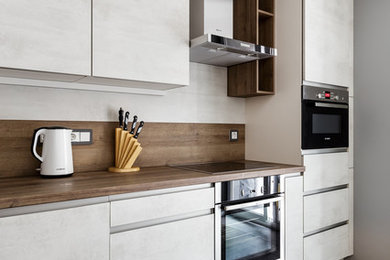 Источник вдохновения для домашнего уюта: кухня в современном стиле с плоскими фасадами, белыми фасадами, серым полом и коричневой столешницей