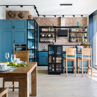 Idée de décoration pour une grand cuisine américaine urbaine en L avec un évier encastré, un placard avec porte à panneau encastré, un plan de travail en surface solide, une crédence rouge, une crédence en brique, un électroménager encastrable, un îlot central, un sol beige, un plan de travail noir, des portes de placard turquoises et un sol en bois clair.