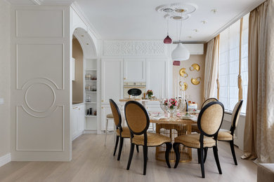 Стильный дизайн: угловая кухня-гостиная в стиле неоклассика (современная классика) с белыми фасадами, белой техникой, светлым паркетным полом и бежевым полом без острова - последний тренд