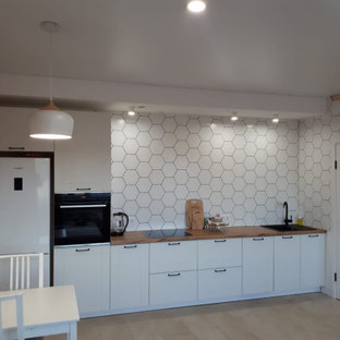 Mid-sized scandinavian single-wall eat-in kitchen in Yekaterinburg with an integrated sink, recessed-panel cabinets, white cabinets, laminate benchtops, white splashback, porcelain splashback, black appliances and brown benchtop.