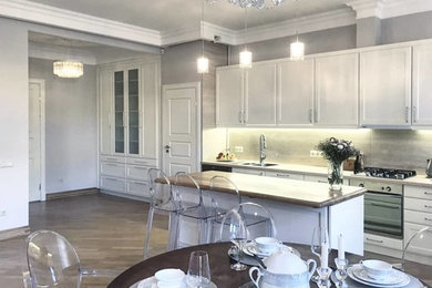 Inspiration for a large traditional galley kitchen/diner in Saint Petersburg with a double-bowl sink, recessed-panel cabinets, white cabinets, marble worktops, beige splashback, marble splashback, stainless steel appliances, medium hardwood flooring, an island and beige worktops.