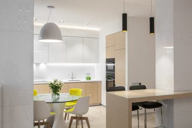 Идея дизайна: угловая кухня-гостиная среднего размера в современном стиле с плоскими фасадами, белым фартуком, черной техникой и бежевым полом