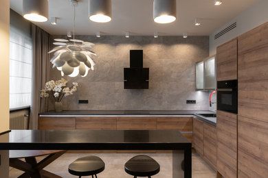 Cette photo montre une cuisine tendance en L et bois brun avec un évier posé, un placard à porte plane, une crédence grise, un électroménager noir, une péninsule, un sol gris et plan de travail noir.