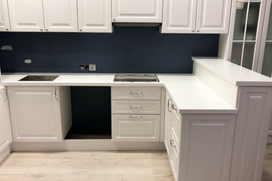 На фото: угловая кухня среднего размера в классическом стиле с фасадами с утопленной филенкой, белыми фасадами, столешницей из акрилового камня, синим фартуком и белой столешницей с