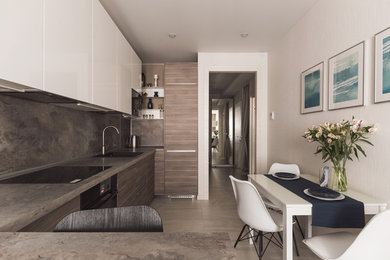 Свежая идея для дизайна: прямая кухня-гостиная в современном стиле с одинарной мойкой, плоскими фасадами, фасадами цвета дерева среднего тона, коричневым фартуком, серым полом и черной техникой - отличное фото интерьера