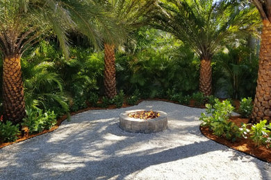 Bild på en tropisk trädgård i delvis sol, med en öppen spis och grus