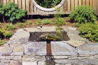 Imagen de jardín clásico de tamaño medio en patio con fuente y adoquines de piedra natural
