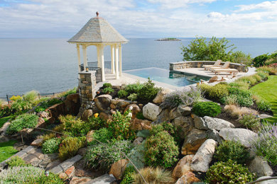 Photo of a mid-sized coastal backyard stone retaining wall landscape.