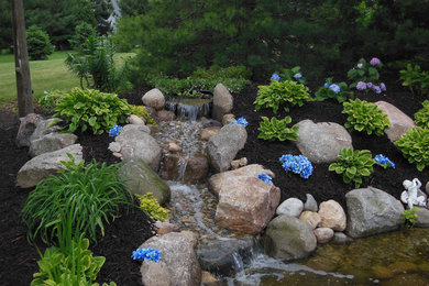 Photo of a mid-sized traditional partial sun backyard stone water fountain landscape in Other for summer.