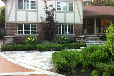 This is an example of a medium sized traditional front driveway partial sun garden for summer in Toronto with a garden path and natural stone paving.