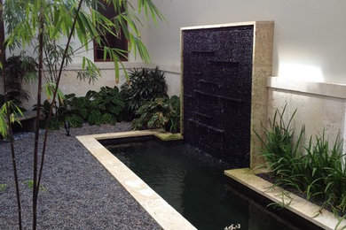This is an example of a mid-sized contemporary full sun backyard stone water fountain landscape in Miami for summer.