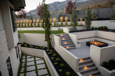 This is an example of a backyard concrete paver and vinyl fence landscaping in Salt Lake City with a fire pit.