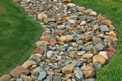 This is an example of a southwestern full sun hillside river rock landscaping in Dallas.