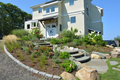 Diseño de jardín costero grande en patio delantero con jardín francés, muro de contención, exposición total al sol y adoquines de piedra natural
