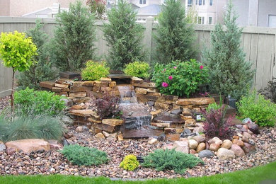 Photo of a mid-sized rustic backyard stone water fountain landscape in Calgary.