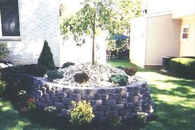Diseño de jardín en patio delantero con muro de contención y adoquines de piedra natural