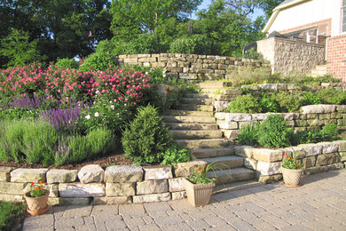 Foto de jardín grande en primavera en patio delantero con muro de contención, exposición parcial al sol y adoquines de piedra natural