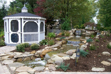 Modelo de jardín clásico renovado de tamaño medio en primavera en patio trasero con fuente, exposición total al sol y adoquines de ladrillo