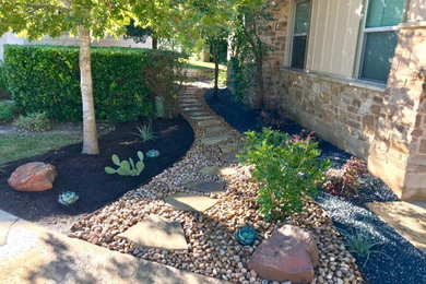 This is an example of a mid-sized contemporary drought-tolerant and partial sun backyard river rock flower bed in Austin.