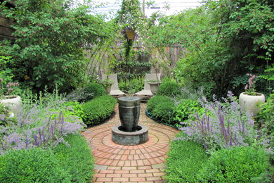 Imagen de jardín tradicional de tamaño medio en patio trasero con fuente, adoquines de ladrillo y jardín francés