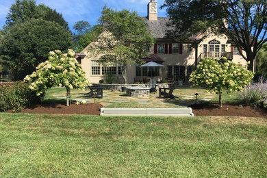 This is an example of a large traditional back full sun garden for summer in Philadelphia with a fire feature and natural stone paving.