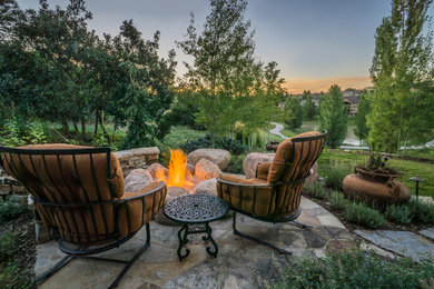 Aménagement d'une grande terrasse arrière classique avec un foyer extérieur et des pavés en pierre naturelle.