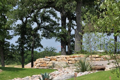 This is an example of an expansive rustic sloped xeriscape garden in Austin with a retaining wall and gravel.