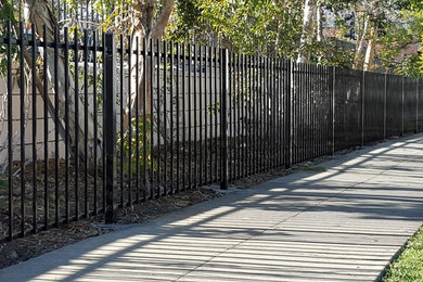 This is an example of a mid-sized industrial drought-tolerant and partial sun front yard mulch and metal fence landscaping in Los Angeles for summer.
