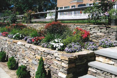 Photo of a mid-sized traditional partial sun backyard stone retaining wall landscape in New York.