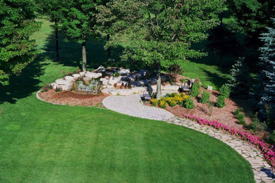Ejemplo de jardín clásico renovado de tamaño medio en patio trasero con jardín francés, fuente y adoquines de ladrillo