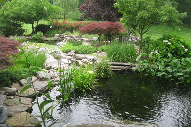 Ejemplo de jardín clásico de tamaño medio en primavera en patio trasero con jardín francés, estanque, exposición parcial al sol y adoquines de piedra natural