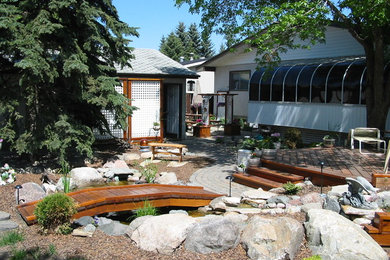 This is an example of a rustic drought-tolerant backyard concrete paver water fountain landscape in Edmonton.
