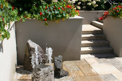 Exempel på en modern trädgård, med en fontän och naturstensplattor
