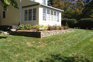 Photo of an expansive traditional back formal full sun garden for spring in Philadelphia with a retaining wall and mulch.