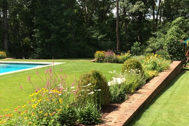 Ejemplo de jardín tradicional de tamaño medio en patio trasero con jardín francés, muro de contención, exposición total al sol y adoquines de ladrillo