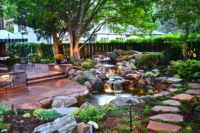 Diseño de jardín clásico en patio trasero con adoquines de piedra natural y cascada