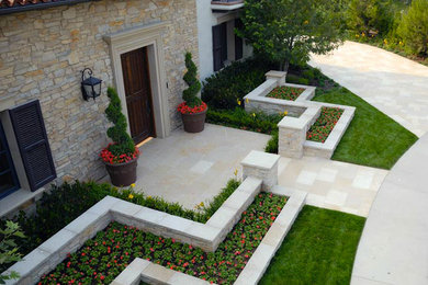 Diseño de jardín clásico renovado en patio delantero con jardín francés, muro de contención y adoquines de piedra natural