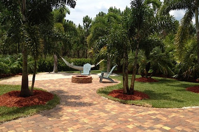 Photo of a mid-sized tropical full sun backyard brick driveway in Miami with a fire pit for summer.