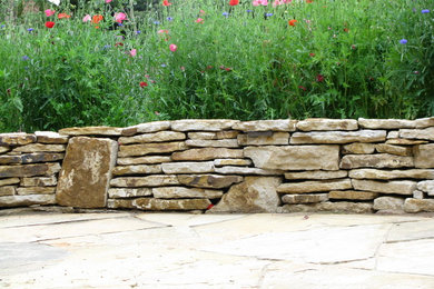 Foto de jardín de tamaño medio en patio trasero con muro de contención, exposición total al sol y adoquines de piedra natural