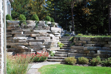 Cette photo montre un grand jardin arrière chic avec un mur de soutènement, une exposition partiellement ombragée et des pavés en pierre naturelle.