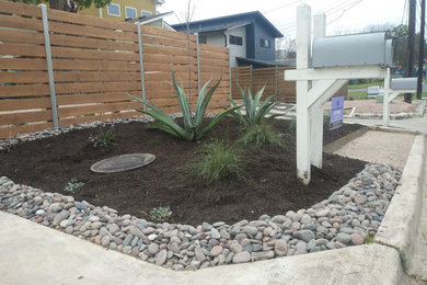 Photo of a contemporary drought-tolerant and full sun front yard wood fence and river rock landscaping in Austin.